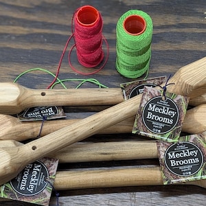 May include: Wooden broom handles with attached tags that read "Meckley Brooms". Two spools of thread, one red and one green, are also present. The items are arranged on a dark wooden surface.