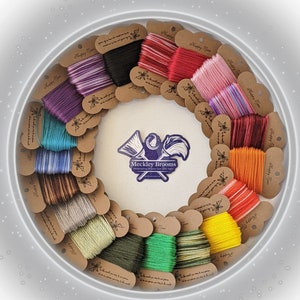 May include: A collection of 16 spools of embroidery floss in various colors, including red, pink, blue, green, and brown. The spools are arranged in a circle around a sticker that says "Meckley Brooms - Handcrafted Brooms Since 1903".