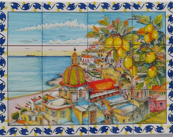 May include: A colorful ceramic tile mural depicting a seaside town with a church dome, buildings, and a lemon tree with ripe fruit. The scene is framed by a blue and yellow border with a leaf pattern.
