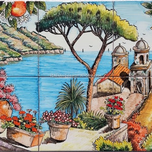 May include: A hand-painted ceramic tile mural depicting a picturesque Italian coastal scene. The mural features a vibrant blue sea, a lush green hillside, a charming village with white buildings, and a large pine tree. The scene is framed by potted flowers and a lemon tree.