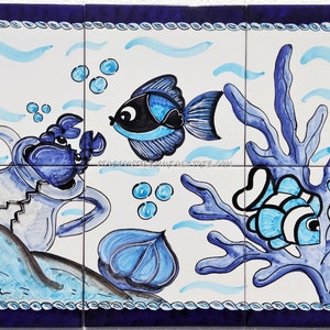 May include: Hand-painted ceramic tile set featuring an underwater scene. The design includes a blue crab, fish, and coral against a white background. The tiles are framed with a dark blue border and rope-like detailing.
