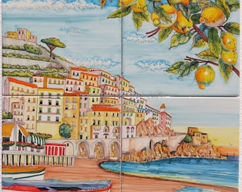 May include: A colorful ceramic tile mural depicting a coastal Italian town with buildings, a harbor, and boats. The town is nestled against a hillside with a lemon tree in the upper right corner. The tile is labeled "AMALFI" in the lower left corner.
