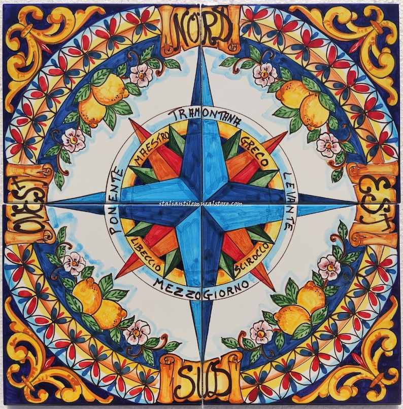 May include: A colourful Italian ceramic tile featuring a compass design. The compass points to the four cardinal directions: North, South, East, and West. The tile is decorated with lemons, flowers, and scrolls.