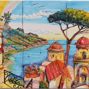May include: A colorful ceramic tile mural depicting a picturesque Italian coastal scene. The mural features a view of a town nestled on a hillside overlooking a blue sea. A lush green pine tree stands in the foreground, with a red-roofed building and the text "KALEIDOS" visible. The text "RAVELLO" is also visible in the lower left corner.