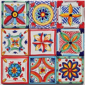 Op de afbeelding: Negen kleurrijke keramische tegels met bloemmotieven. De tegels zijn gerangschikt in een 3x3 raster. Elke tegel heeft een ander ontwerp met een mix van rood, geel, blauw, groen en wit.