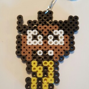 May include: A brown and black beaded keychain with a yellow beaded figure attached. The figure has a white face with two black eyes.