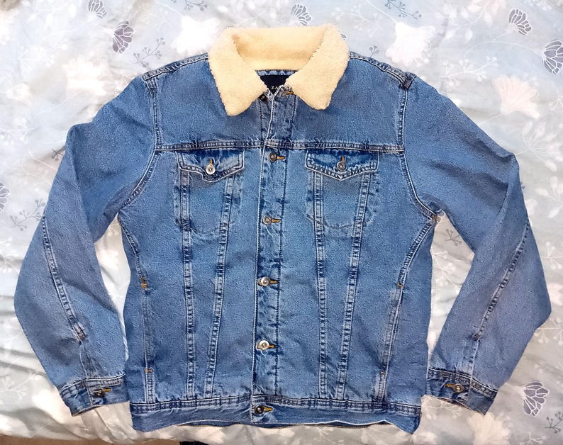 May include: A light blue denim jacket with a cream-coloured, fluffy collar. The jacket features two chest pockets, button fastenings, and a classic design. This outerwear is suitable for casual wear.