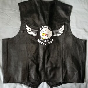 Può includere: Giubbotto da motociclista in pelle nera con una toppa ricamata bianca e nera che dice "Southern Cruisers Riding Club" e presenta un'aquila bianca con un becco rosso.