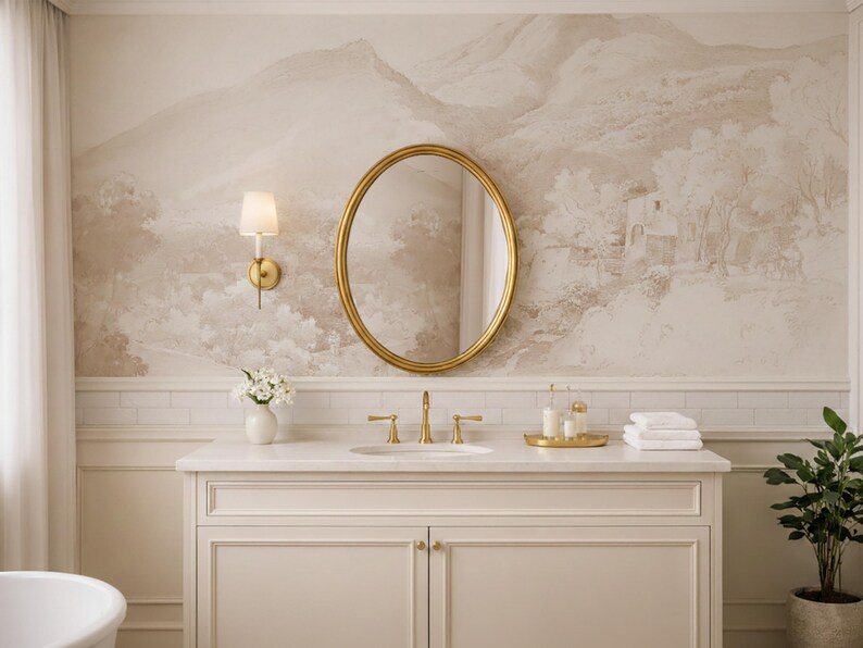 May include: A bathroom interior with a gold oval mirror, white vanity unit with gold taps, and a landscape mural. A small vase of white flowers sits on the vanity, along with toiletries and white towels. A potted plant is in the corner.