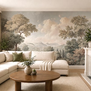 Puede incluir: Un mural de pared con una pintura de paisaje de colinas onduladas, árboles densos y un cielo nublado en tonos tierra apagados. El mural se muestra detrás de un sofá seccional color crema, una mesa de centro redonda de madera y una chimenea blanca.