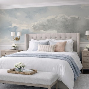 May include: A bedroom with a large bed, nightstands, and a bench. The bed has a tufted headboard and is covered with white linens, pillows, and a blue blanket. The wall behind the bed features a mural of a cloudy sky.