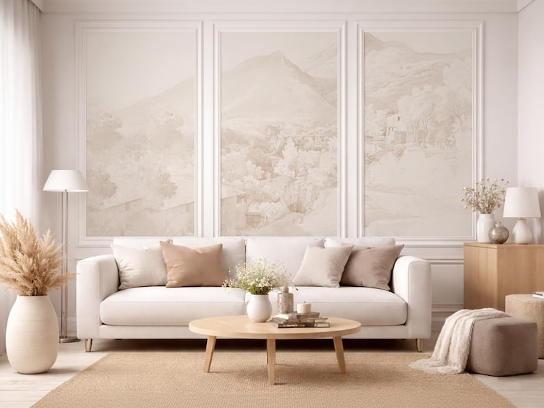 May include: A living room interior with a white sofa, beige cushions, and a round wooden coffee table. The wall features three framed landscape paintings in neutral tones. A beige rug, floor lamp, vase with pampas grass, and side table complete the scene.