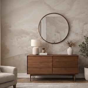 May include: A stylish bedroom interior featuring a wooden chest of drawers, a round mirror, a table lamp, and a potted plant. The wall has a neutral-toned mural of a landscape. The chest of drawers is approximately 150 cm wide.