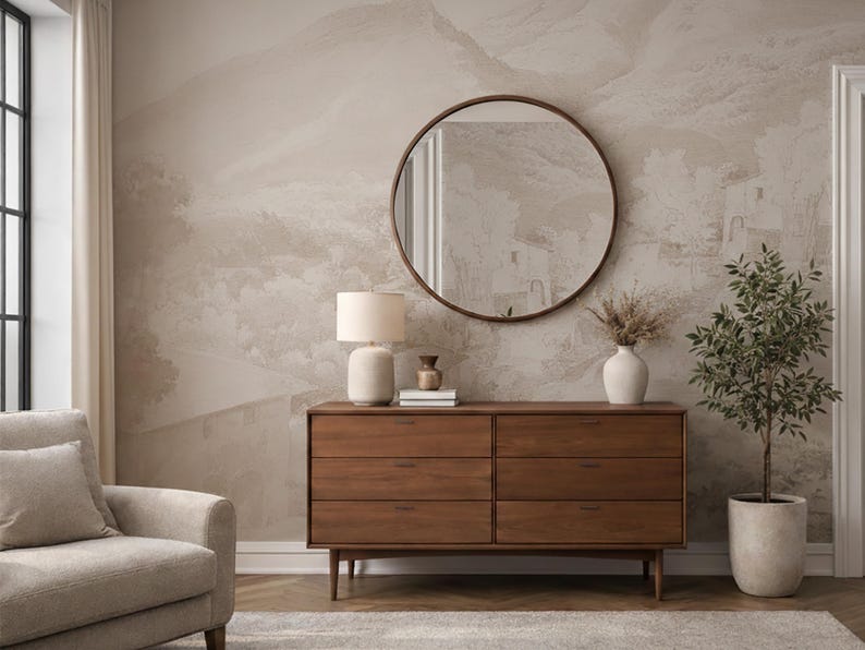 May include: A stylish bedroom interior featuring a wooden chest of drawers, a round mirror, a table lamp, and a potted plant. The wall has a neutral-toned mural of a landscape. The chest of drawers is approximately 150 cm wide.