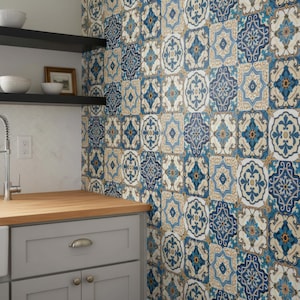 May include: A kitchen with a white sink, gray cabinets, and a wooden countertop. The backsplash features patterned tiles in shades of blue, white, and tan. Black shelves hold white bowls and a framed picture.