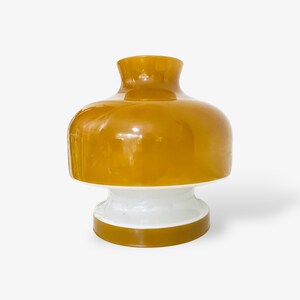 Peut inclure: Un vase en céramique avec un corps large et rond et une base blanche. Le vase est d'un jaune moutarde foncé avec une bande blanche autour de la base.