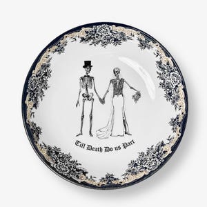 Może przedstawiać: Biała ceramiczna miska z czarnym i złotym wzorem kwiatowym. Miska przedstawia parę szkieletów w sukni ślubnej i smokingu z napisem "Till Death Do Us Part".