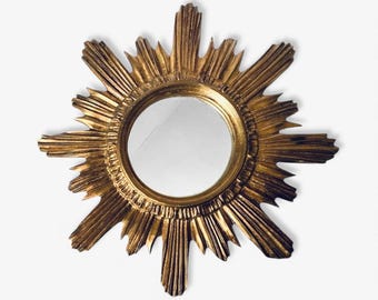Può includere: Uno specchio a forma di sole dorato con un centro rotondo e riflettente. La cornice dello specchio presenta un design strutturato e radiante, creando un aspetto solare. Lo specchio è un elemento decorativo da parete.