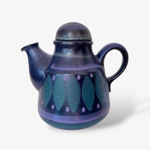 Könnte beinhalten: Eine dunkelblaue Keramik-Teekanne mit passendem Deckel, verziert mit einem wiederkehrenden Muster aus türkisfarbenen Rauten und kleinen hellvioletten Punkten um die Mitte. Die Teekanne hat einen geschwungenen Henkel, einen kurzen Ausguss und eine glatte Glasur.