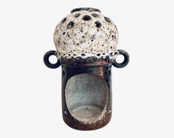 Könnte beinhalten: Ein brauner und weißer Kerzenhalter aus Keramik mit runder Oberseite und zylindrischem Sockel. Die Oberseite hat ein Muster aus kleinen Löchern und der Sockel eine große Öffnung für eine Kerze.