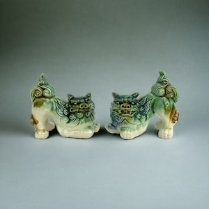 Könnte beinhalten: Ein Paar grüne, glasierte Keramik-Foo-Hunde, traditionelle chinesische Wächterlöwen, mit detaillierten Schnitzereien und einem weißen Sockel.