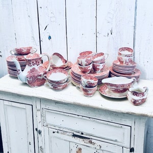 Könnte beinhalten: Ein Vintage-Set aus Porzellan-Teetassen und Untertassen mit einem roten und weißen Blumenmuster. Das Set beinhaltet eine Teekanne, eine Milchkännchen, eine Zuckerdose und mehrere Tassen und Untertassen.