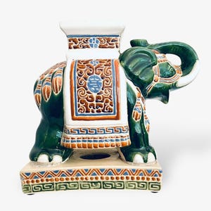 May include: A ceramic elephant figurine in green, white, and brown. The elephant has detailed patterns on its back and base, with a decorative saddle and a raised platform. The figurine is a decorative item.