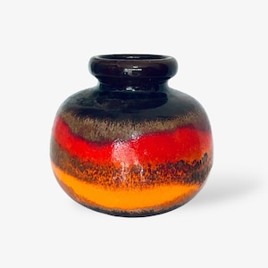 Puede incluir: Un jarrón pequeño y redondo de cerámica con un esmalte marrón, naranja y rojo. El jarrón tiene una boca ancha y una base estrecha.