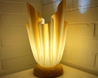 May include: A cream-colored table lamp with a unique, pleated, ruffled shade. The lamp base is a warm, light brown color.