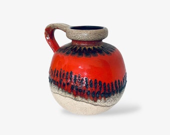 May include: A red and white ceramic vase with a brown handle. The vase has a textured surface and a geometric design.