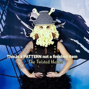 Può includere: Uno schema all'uncinetto per un cappello ispirato a Cthulhu con un cappello grigio, tentacoli gialli e due occhi verdi. Il testo "This is a PATTERN not a finished item" e "The Twisted Hatter" è visibile nell'immagine.