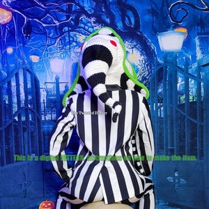 May include: A black and white striped suit with a green and white crocheted hat. The hat is shaped like a long, pointed cone with a red pom-pom on top. The suit is sitting on a white skull. The background is a blue and green Halloween-themed backdrop with pumpkins and a gate.