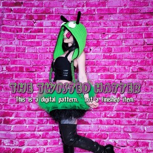May include: A green crochet hat with a cartoon face and a green tutu skirt. The text "THE TWISTED HATTER" is written in green letters on a pink brick wall. The text "This is a digital pattern, not a finished item." is written below the title.
