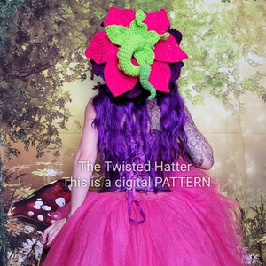 May include: A pink and purple crocheted flower hat with a green crocheted dragon on top. The hat is worn by a person with purple hair and a pink tulle skirt. The text "The Twisted Hatter This is a digital PATTERN" is visible on the image.