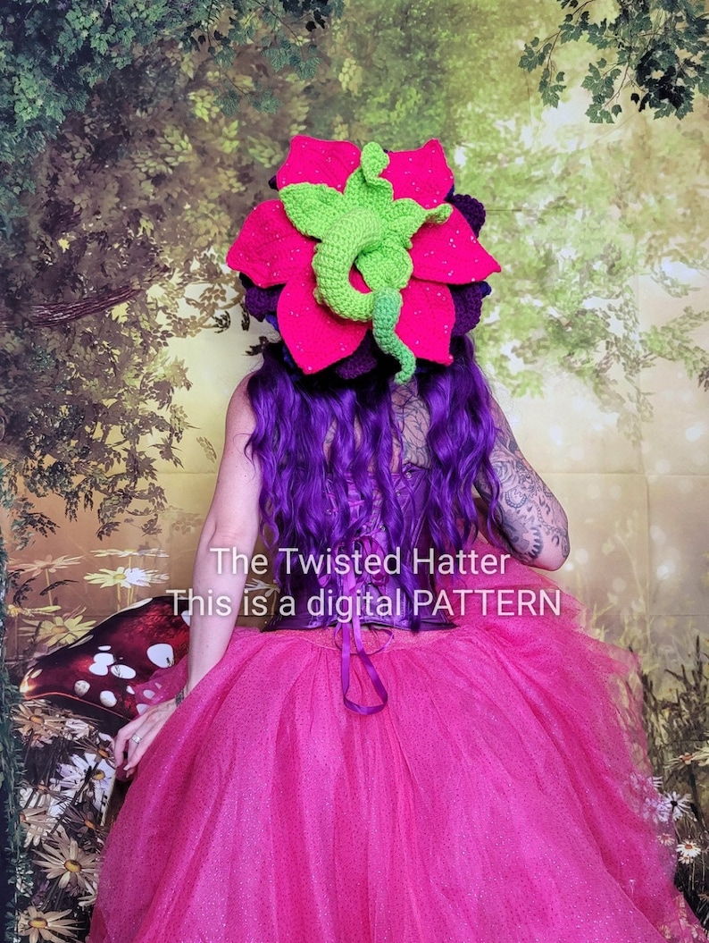 May include: A pink and purple crocheted flower hat with a green crocheted dragon on top. The hat is worn by a person with purple hair and a pink tulle skirt. The text "The Twisted Hatter This is a digital PATTERN" is visible on the image.