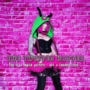 May include: A woman wearing a green and pink hooded hat with a creature design, a black top, a pink tutu, and black boots. The background is a pink brick wall. The text "THE TWISTED HATTER" and "This is a digital pattern, not a finished item." is displayed below the woman.