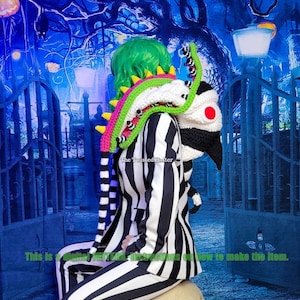 May include: A black and white striped suit with a green, pink and white crocheted scarf. The scarf is shaped like a monster with a red eye. The text "The Twisted Hatter" is visible on the scarf.