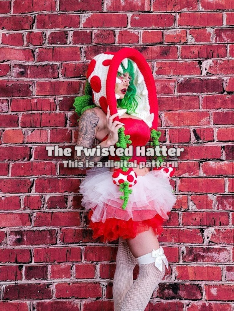 May include: A woman wearing a crocheted green and red plant costume with a white tutu and white stockings. The costume is inspired by a video game character. The text "The Twisted Hatter This is a digital pattern" is visible in the image.