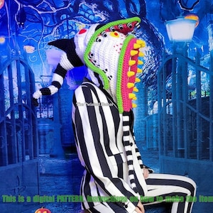 May include: A crochet pattern for a colourful, whimsical hat featuring a large, toothy mouth with eyes and a long, striped tail. The hat is worn by a person in a black and white striped suit, sitting on a white, skull-shaped stool. The background is a blue and green forest scene with a gate and a street lamp.