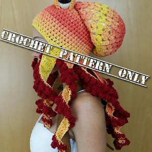 Op de afbeelding: Een gehaakte octopusmuts met een rood-geel ombre-ontwerp. De muts heeft een grote, ronde kop met &eacute;&eacute;n oog en een lange, stromende staart met tentakels.