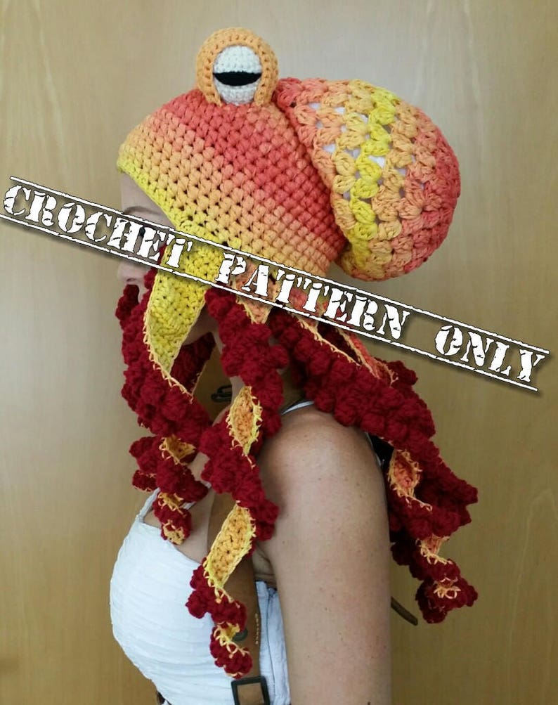 Op de afbeelding: Een gehaakte octopusmuts met een rood-geel ombre-ontwerp. De muts heeft een grote, ronde kop met &eacute;&eacute;n oog en een lange, stromende staart met tentakels.