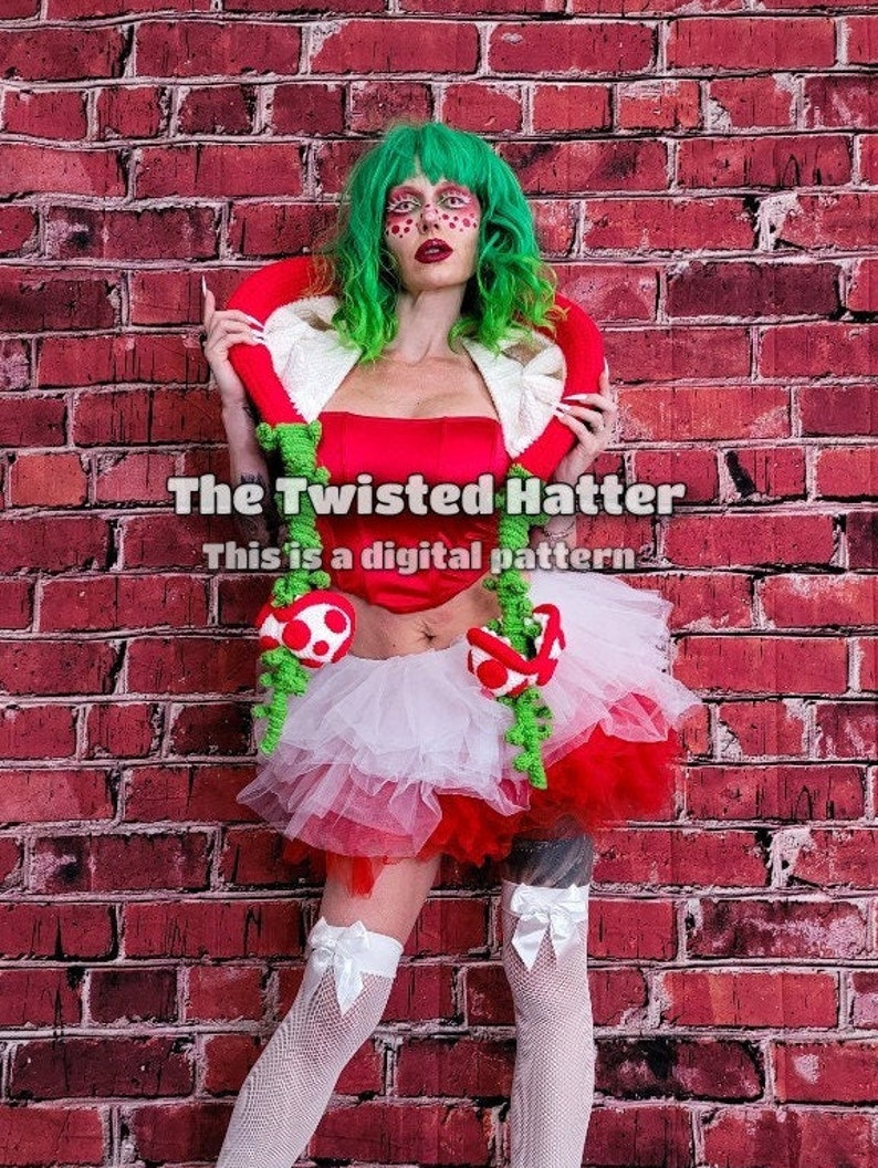May include: A woman wearing a red and white tutu with green mushroom accents and a red and white top with a green crocheted collar. The text "The Twisted Hatter" and "This is a digital pattern" is visible in the image.