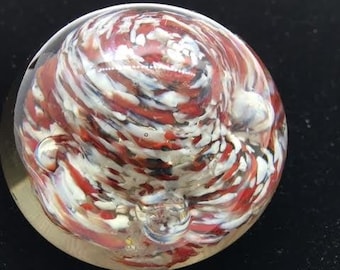 May include: A red, white, and black glass paperweight with a swirling pattern.