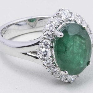 Puede incluir: Un anillo de plata con una gran esmeralda ovalada rodeada por un halo de diamantes m&aacute;s peque&ntilde;os.