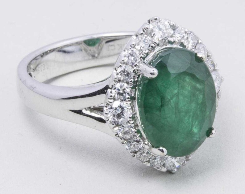 Puede incluir: Un anillo de plata con una gran esmeralda ovalada rodeada por un halo de diamantes m&aacute;s peque&ntilde;os.