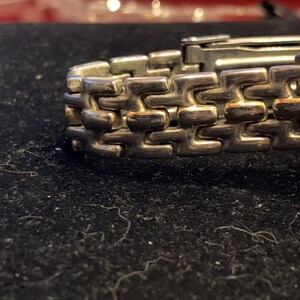 Peut inclure: Gros plan sur un bracelet de montre argent&eacute; avec un accent dor&eacute;. Le bracelet est compos&eacute; de maillons entrelac&eacute;s.