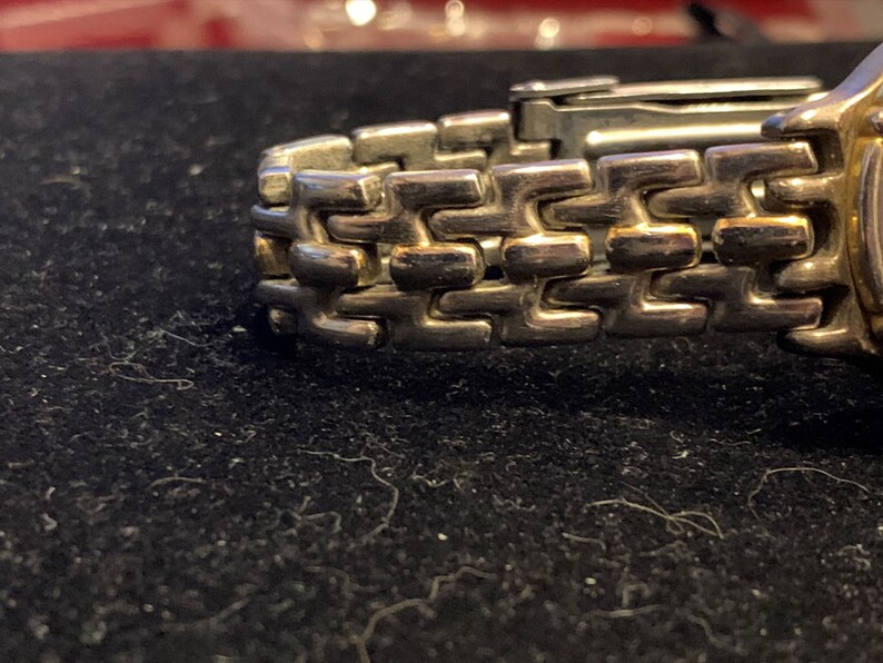 Peut inclure: Gros plan sur un bracelet de montre argent&eacute; avec un accent dor&eacute;. Le bracelet est compos&eacute; de maillons entrelac&eacute;s.