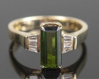 May include: A gold ring with a green emerald-cut gemstone and two smaller diamond accents on either side.
