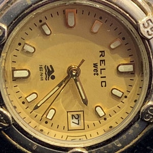Peut inclure: Une montre-bracelet dor&eacute;e avec un cadran de couleur cr&egrave;me. Le cadran de la montre comporte des marques noires et des index blancs. Le cadran de la montre comporte &eacute;galement une fen&ecirc;tre de date &agrave; 3 heures et les mots "RELIC wet" imprim&eacute;s sur le cadran. La montre est &eacute;tanche &agrave; 165 pieds.