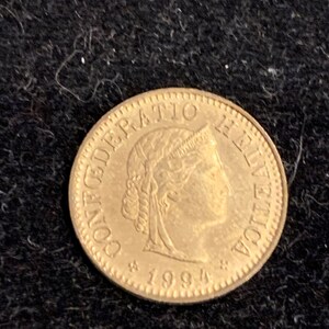 Puede incluir: Una moneda de color dorado con la inscripci&oacute;n "CONFEDERATIO HELVETICA" y el a&ntilde;o "1994" alrededor del borde.